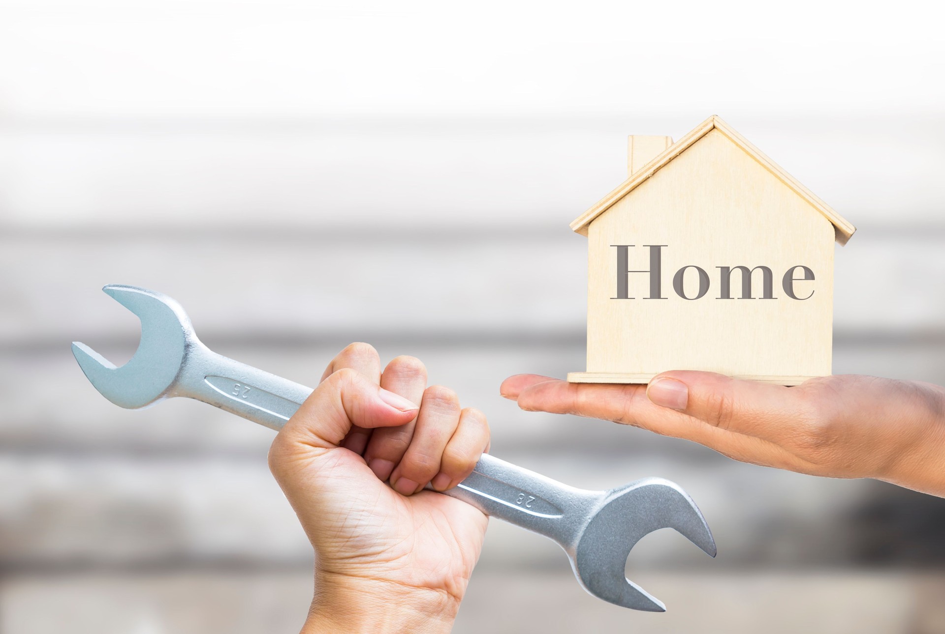 Wooden house model in girl hand with wrench in hand over blurred wooden wall background