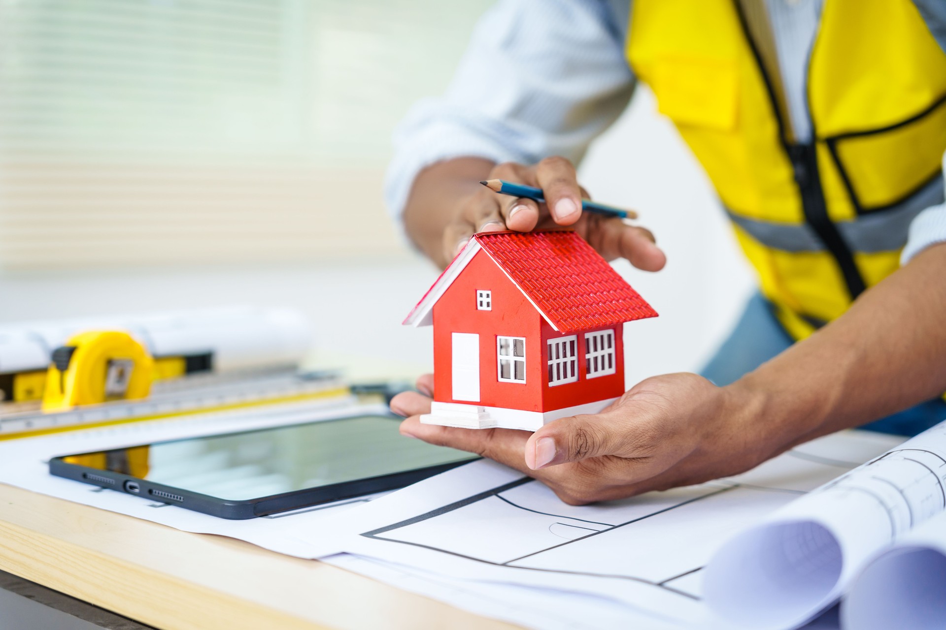 Asian male architect works at desk with house model toy and A3 paper blueprints, construction real estate law, zoning, permits, and resolving property disputes through arbitration and litigation.